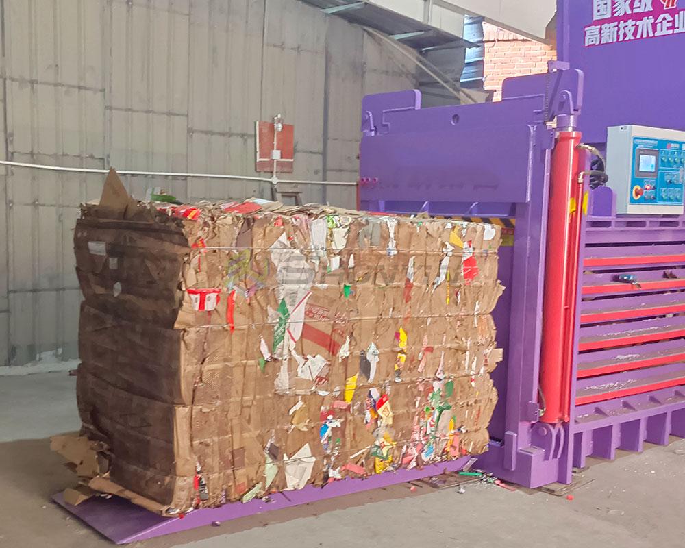 Large hydraulic baler compressing waste cardboard with conveyor for efficient recycling.