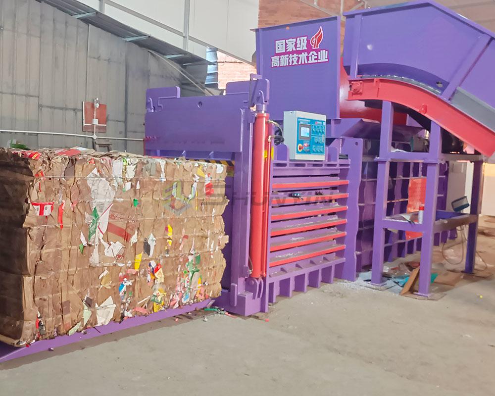 Industrial hydraulic baler with conveyor compressing cardboard into dense bales for recycling.